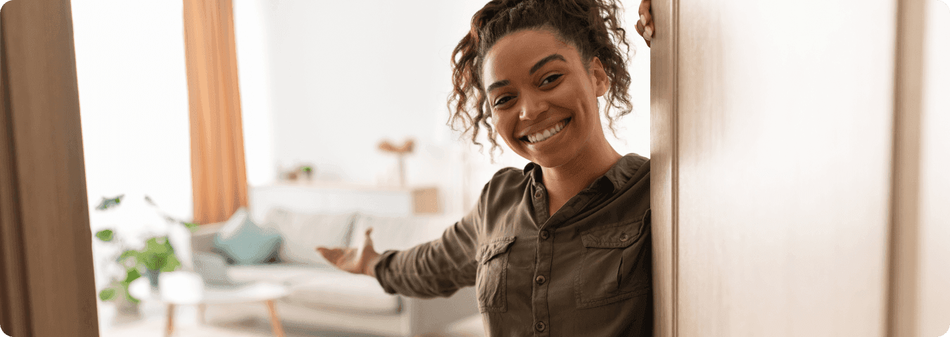 Mulher sorridente abrindo a porta e recebendo calorosamente alguém em uma sala aconchegante e bem decorada, simbolizando a hospitalidade em um aluguel de temporada.